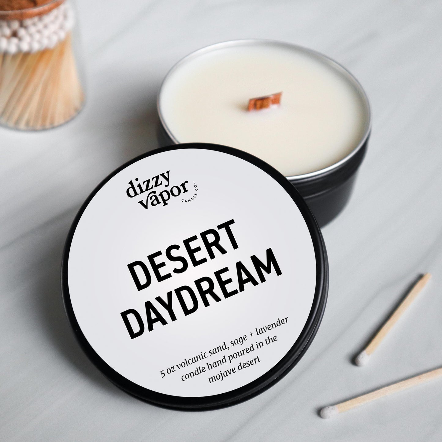 Candle labeled 'Desert Daydream' by dizzy vapor on a light gray surface.