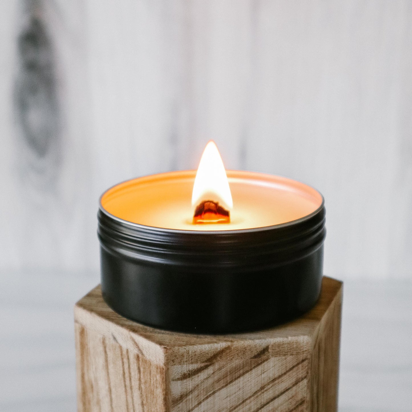 Candle in a black container on a wooden stand with a blurred background
