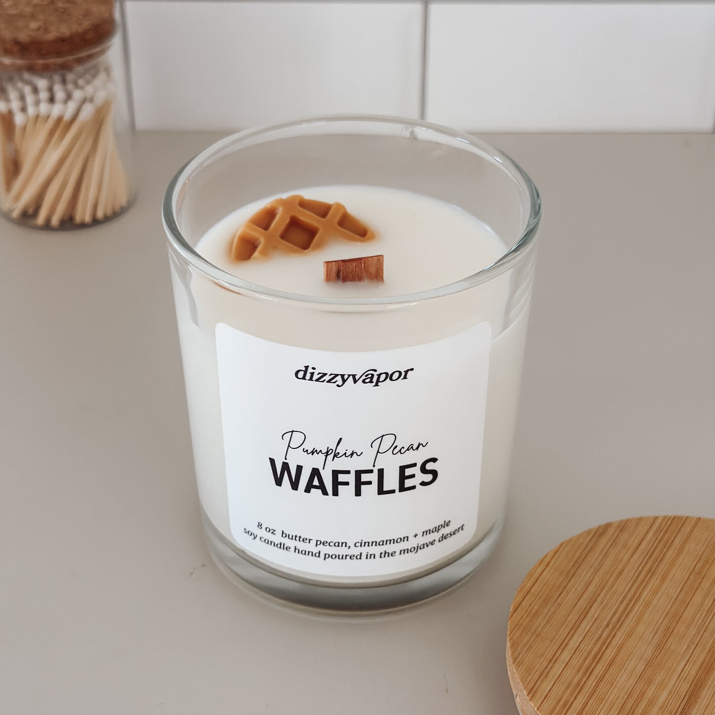 Candle with waffle decorations and 'dizzyvapor' branding on a neutral background
